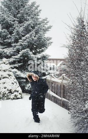 Ragazzo felice che indossa un cappotto con cappuccio in pelliccia all'aperto nella neve il giorno d'inverno. Foto Stock