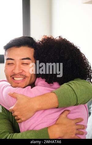 Uomo asiatico che abbraccia la sua ragazza latina a casa. Foto Stock