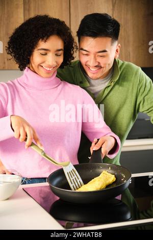 Coppia multietnica cucinare omelette insieme in cucina. Foto Stock