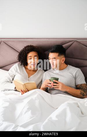 Coppie multirazziali che imparano le lingue con un libro a letto insieme. Foto Stock