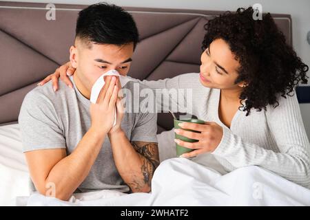 Uomo asiatico che soffia il naso in un fazzoletto e sua moglie latina che si prende cura. Foto Stock