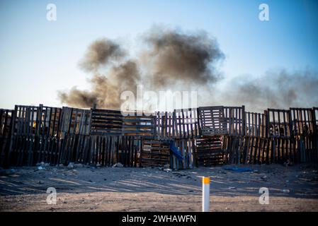 Barricate fatte di vecchi pallet di legno separano la strada dagli incendi accidentali con fumo nero come se fossero zone di guerra che separano i disastri in Perù Foto Stock