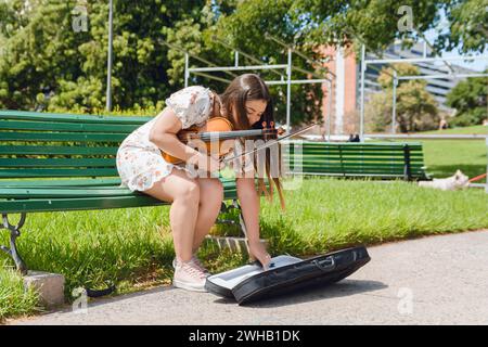 giovane donna venezuelana latina, violinista, artista di strada, che mette la custodia per violino sul pavimento per soldi mentre gioca, copia spazio. Foto Stock