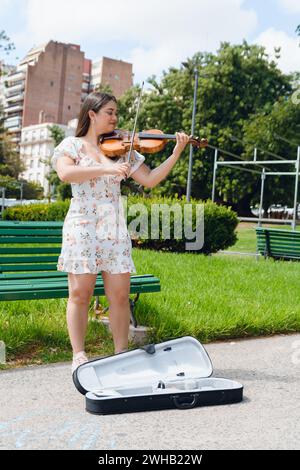 immagine verticale di una giovane donna di busker latina violinista che indossa un abito, capelli lunghi, ha ispirato un felice gioco per strada, facendo musica e lavorando, copiando spazio. Foto Stock