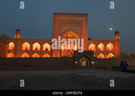 KHIVA, UZBEKISTAN - 7 SETTEMBRE 2022: L'antica madrasa Allakuli Khan con illuminazione arancione in tarda serata Foto Stock
