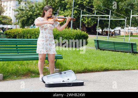 immagine verticale di una giovane donna di busker latina violinista che indossa un abito, capelli lunghi, ha ispirato un felice gioco per strada, facendo musica e lavorando, copiando spazio. Foto Stock