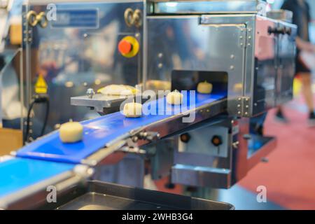 Immagine ravvicinata di un sistema automatizzato di trasformazione alimentare industriale che mostra porzioni di impasto su un nastro trasportatore blu, con elementi di macchinari sul retro Foto Stock