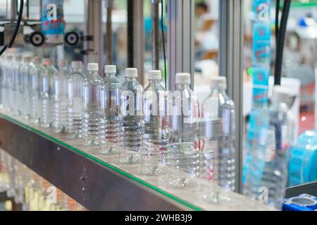 Immagine che mostra una fila di bottiglie d'acqua in plastica trasparente su un nastro trasportatore in un impianto di imbottigliamento, con particolare attenzione alle bottiglie e ai macchinari industriali i. Foto Stock