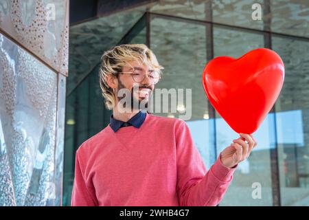 Giovane sorridente in piedi con un palloncino a forma di cuore. Amore Foto Stock