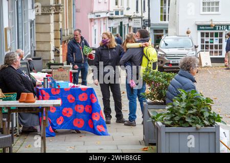 Il giorno del mercato in una città del Suffolk sul marciapiede, un volontario prende donazioni in aiuto del Poppy Day per la Royal British Legion Foto Stock