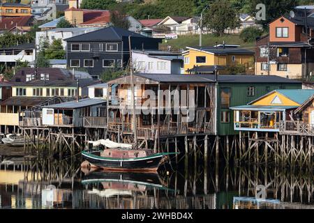 Una barca a vela di fronte alle colorate palafitte, i cosiddetti palafitos, della capitale Castro sull'isola di Chiloe in Cile. Foto Stock