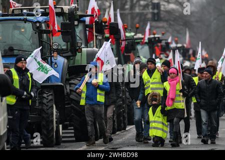 Poznan, Polonia, 9 febbraio 2024. Gli agricoltori della regione della grande Polonia nella Polonia occidentale camminano con le bandiere polacche davanti ai loro trattori mentre bloccano la strada Aleja Niepodleglosci nel centro di Poznań, la capitale della grande Polonia durante lo sciopero degli agricoltori a livello nazionale. La protesta in Polonia fa parte della protesta degli agricoltori europei contro i regolamenti del Green Deal dell'UE. Gli agricoltori polacchi chiedono inoltre una modifica dell'accordo UE con l'Ucraina in merito all'importazione di prodotti agricoli nell'UE. La protesta a Poznań, la capitale della grande Polonia, fu organizzata da Rola Wielkopolska e. Foto Stock