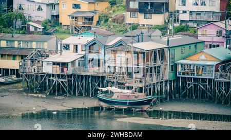 Bassa marea, la barca a vela si trova sulla terraferma di fronte alle colorate palafitos della capitale Castro sull'isola di Chiloe. Foto Stock