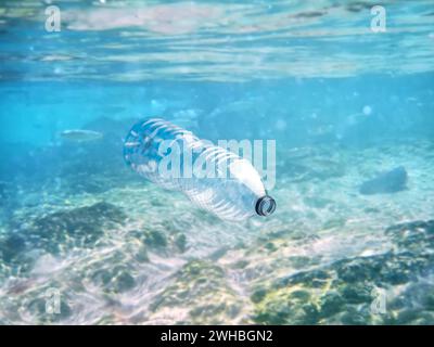 Una bottiglia di plastica monouso galleggia nell'oceano blu cristallino mentre un pesce scivola. (Questa bottiglia è stata raccolta e portata fuori dall'oceano) Foto Stock