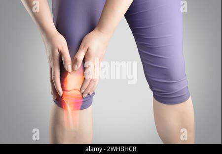 Foto in studio di una giovane donna sportiva che soffre di un infortunio al ginocchio con sfondo grigio Foto Stock