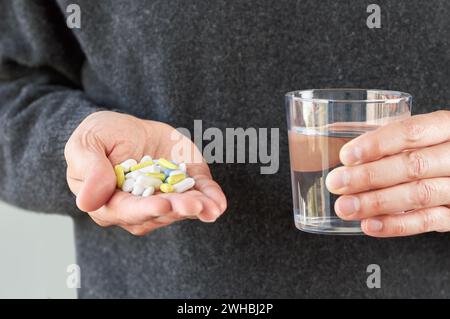 Foto di una mano di un giovane irriconoscibile che mostra molte pillole e un bicchiere d'acqua Foto Stock