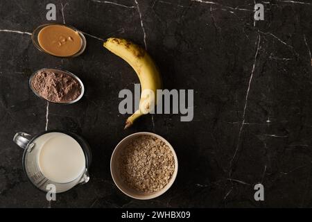 Ingredienti per un frullato ricco di proteine: Banana fresca, avena arrotolata, latte cremoso e polvere di proteine del cioccolato, in modo artistico su un lussuoso Foto Stock