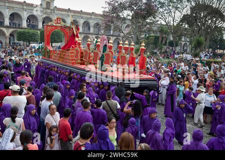 Antigua, Guatemala. Spettatori, famiglia e turisti osservano i ragazzi adolescenti che portano un galleggiante in una processione religiosa durante la settimana Santa, la Semana San Foto Stock