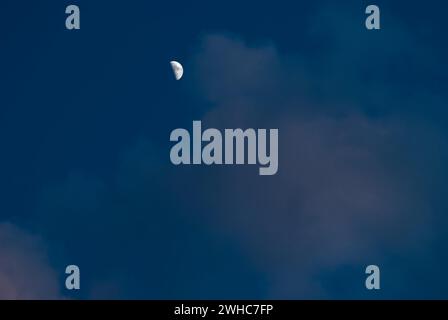 La mezzaluna cerata si erge luminosa in un cielo notturno blu profondo con nuvole di cumulus illuminate leggermente di rosa dal sole, bassa Sassonia, Germania Foto Stock