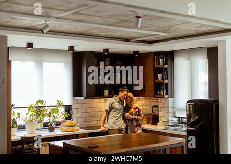 Una scena emozionante si svolge in una cucina domestica mentre una coppia condivide un affettuoso abbraccio, circondato dalla tranquillità della propria casa alla fine di Foto Stock