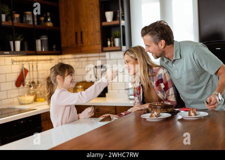 Una scena emozionante si svolge mentre una famiglia assaggia insieme una deliziosa torta al cioccolato nel calore della sua cucina soleggiata, condividendo sorrisi e sorrisi Foto Stock