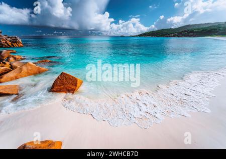 Dolce onda di schiuma sulla spiaggia di Grand Anse, la Digue, Seychelles. Nuvole bianche, mare cristallino, scenario di vacanza. Foto Stock