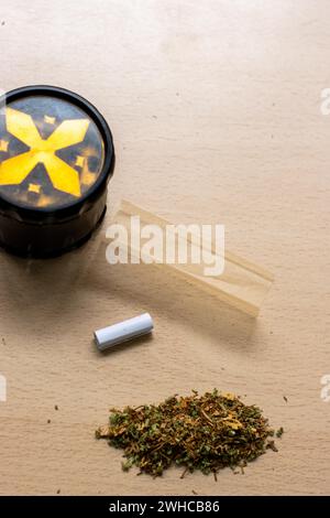 Preparazione di un tema di concetto paraphernalia articolare e droga con trave di erbe utilizzata per macinare i boccioli di cannabis e rotolare le articolazioni di marijuana, accanto alla carta in rotolo Foto Stock