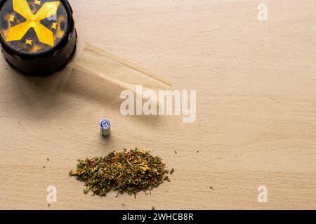 Preparazione di un tema di concetto paraphernalia articolare e droga con trave di erbe utilizzata per macinare i boccioli di cannabis e rotolare le articolazioni di marijuana, accanto alla carta in rotolo Foto Stock