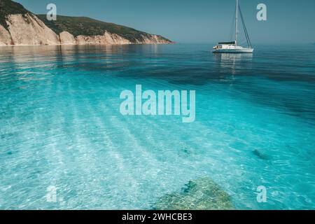 Blu azzurro laguna con calma le onde e drift catamarano a vela yacht barca. Scogliera rocciosa costa in background. Foto Stock