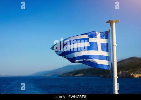 Bandiera della Grecia che sventola sul mare con le pecore da crociera di fronte alla splendida costa. Foto Stock