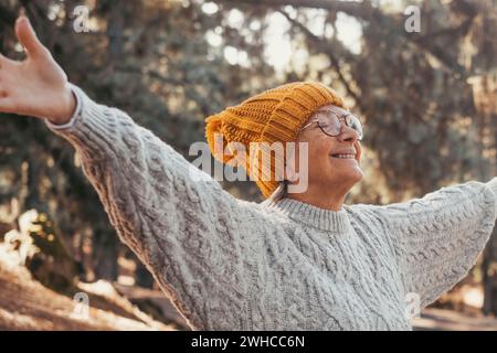 Ritratto, primo piano di una donna di mezza età che si gode e si rilassa seduto a tavola nella natura nella foresta di montagna. Donna anziana che apre le braccia e chiude gli occhi, sentendosi libera. Concetto di libertà stile di vita. Foto Stock