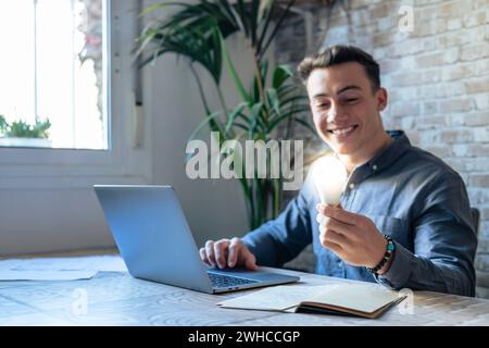 Primo piano del lavoro di un dipendente maschio al computer con una lampadina luminosa brillante ottenere un'idea di business brillante. L'uomo d'affari o il lavoratore si sentono motivati dal successo del progetto di avvio in ufficio. Concetto di innovazione. Foto Stock