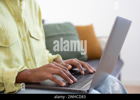 Lavoratrice africana che lavora con un notebook, digita con la tastiera. Donna con le mani in primo piano. Donna d'affari in un ambiente informale e professionale che lavora a tavola, usa l'app online, chatta, scrive articolo. Colpo ritagliato Foto Stock