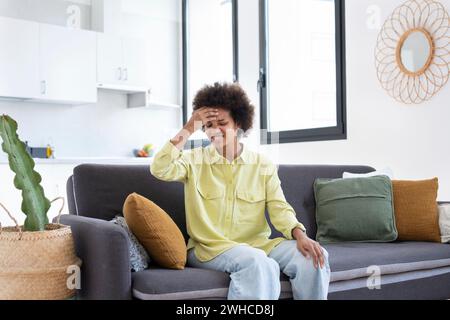 I templi di massaggio della giovane donna africana stressati e turbati sentono un forte concetto di mal di testa, frustrata stanca ragazza nera che tocca la testa dolorante soffre di ipertensione emicranica seduta sul divano di casa Foto Stock