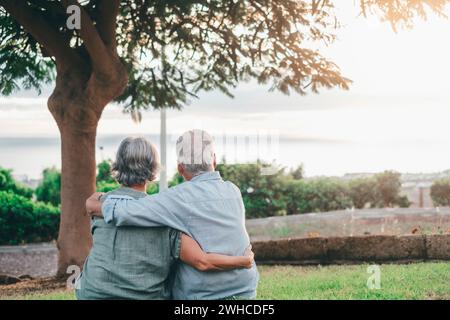 Foto della testa Ritratto ravvicinato donna di mezza età dai capelli grigi felice che si accoccia al marito più anziano sorridente, godendosi un momento tenero al parco. Una vecchia coppia di famiglie che abbraccia e guarda il tramonto. Foto Stock