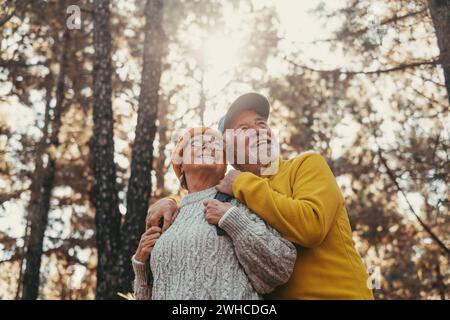 Ritratto, primo piano di gente allegra di mezza età che sorride e guarda gli alberi della foresta intorno a loro. Attiva coppia di anziani che camminano e camminano insieme in montagna divertendosi. Foto Stock