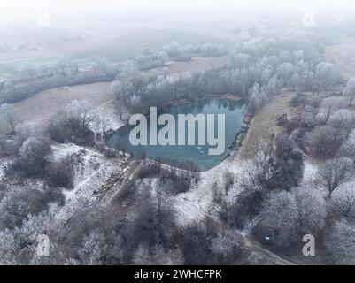 Veduta aerea di un piccolo lago circondato dal gelo invernale in un paesaggio tranquillo, Gechingen, Foresta Nera, Germania Foto Stock
