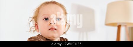 adorabile bambino che guarda lontano dalla culla nella confortevole cameretta di casa, con striscione orizzontale Foto Stock