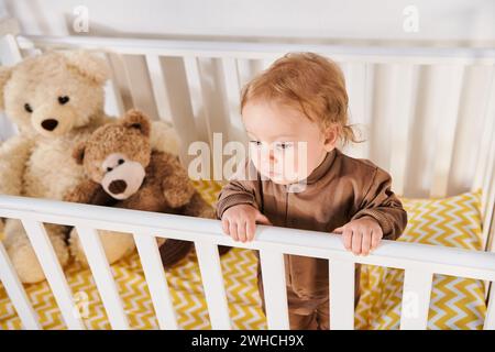 vista ad angolo alto del bambino nella culla accanto ai giocattoli morbidi nella cameretta Foto Stock