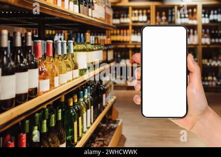Smartphone con schermo vuoto nella mano della donna di fronte al negozio di alcolici. Ordinazione online e shopping di bevande alcoliche. Mockup per app mobile. Foto Stock