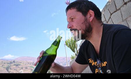 Uomo barbuto che beve una birra in bottiglia per strada Foto Stock