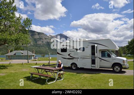 Donna seduta di fronte a un camper presso il campeggio Waterton Townsite, Waterton Lakes National Park, Alberta, Canada Foto Stock