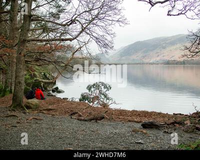 Una coppia seduta, una in giacca rossa, che guarda sulla tranquilla scena di Derwentwater nel Lake District inglese. Concetto: Pace, consapevolezza, calma Foto Stock
