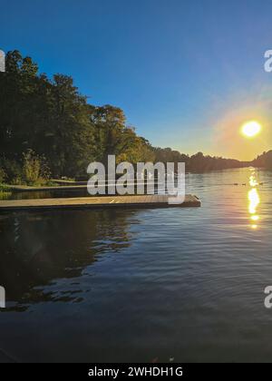 Vista sull'acqua della piccola Wannsee fino a un moderno molo sulla riva retroilluminato dal sole serale Foto Stock