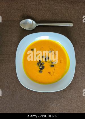 Zuppa di zucca fresca fatta in casa guarnita con semi di zucca e olio di lino come condimento in un piatto bianco con un cucchiaio Foto Stock