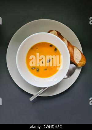 Zuppa di zucca fresca fatta in casa guarnita con semi di zucca e olio di lino come condimento e pretzel stik su un piatto con ciotola per zuppa e cucchiaio Foto Stock