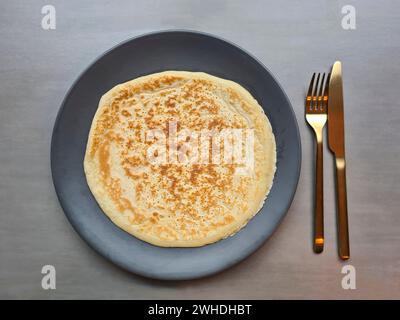 Frittelle su un piatto grigio con posate dorate, piatto a base di uova con coltello e forchetta Foto Stock