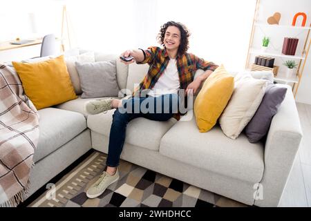 Foto a figura intera di un ragazzo allegro e rilassante indossa una camicia a quadri mentre guardi un film in casa Foto Stock