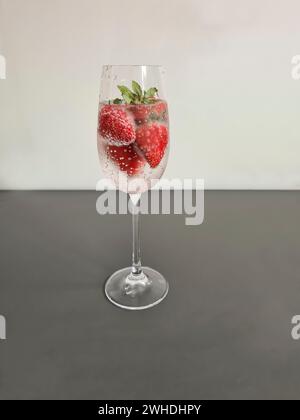 Fragole fresche rosse intere mature con acqua minerale in un bicchiere di champagne come bevanda rinfrescante analcolica in estate Foto Stock