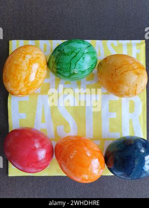 Uova bollite colorate nei colori giallo verde blu e rosso giacciono su un tovagliolo giallo con scritta bianca per Pasqua Foto Stock